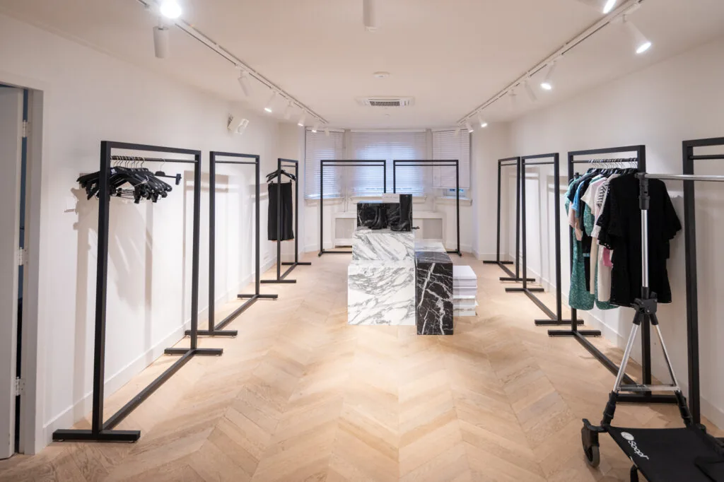 Minimalistisch ingerichte kledingwinkel aan de Hobbemastraat met zwarte kledingrekken en een marmeren toonbank.