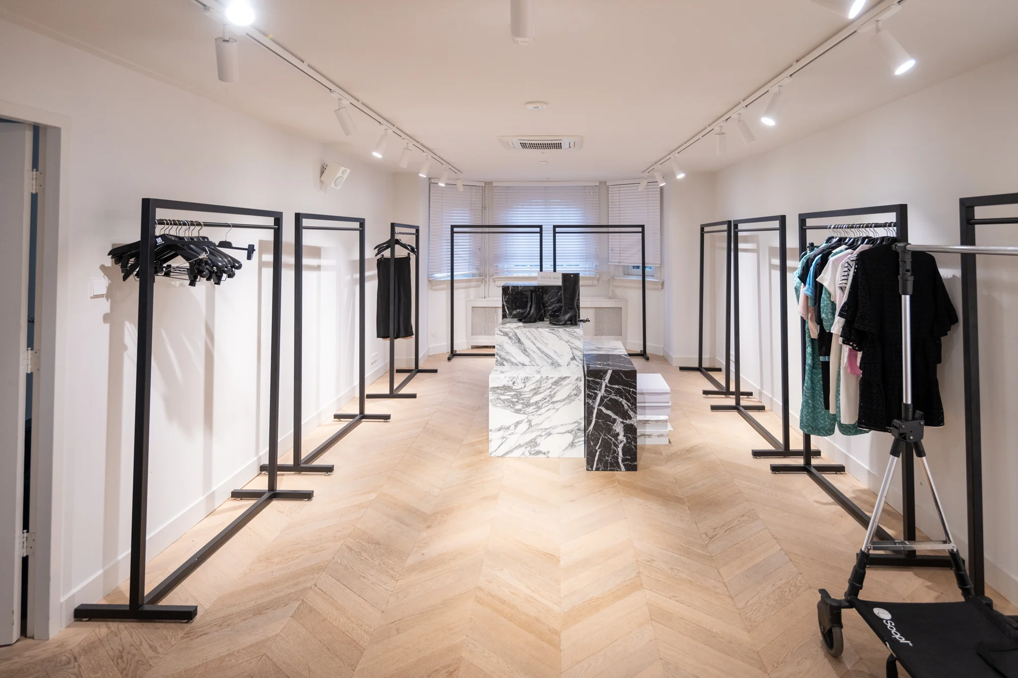 Minimalistisch ingerichte kledingwinkel aan de Hobbemastraat met zwarte kledingrekken en een marmeren toonbank.