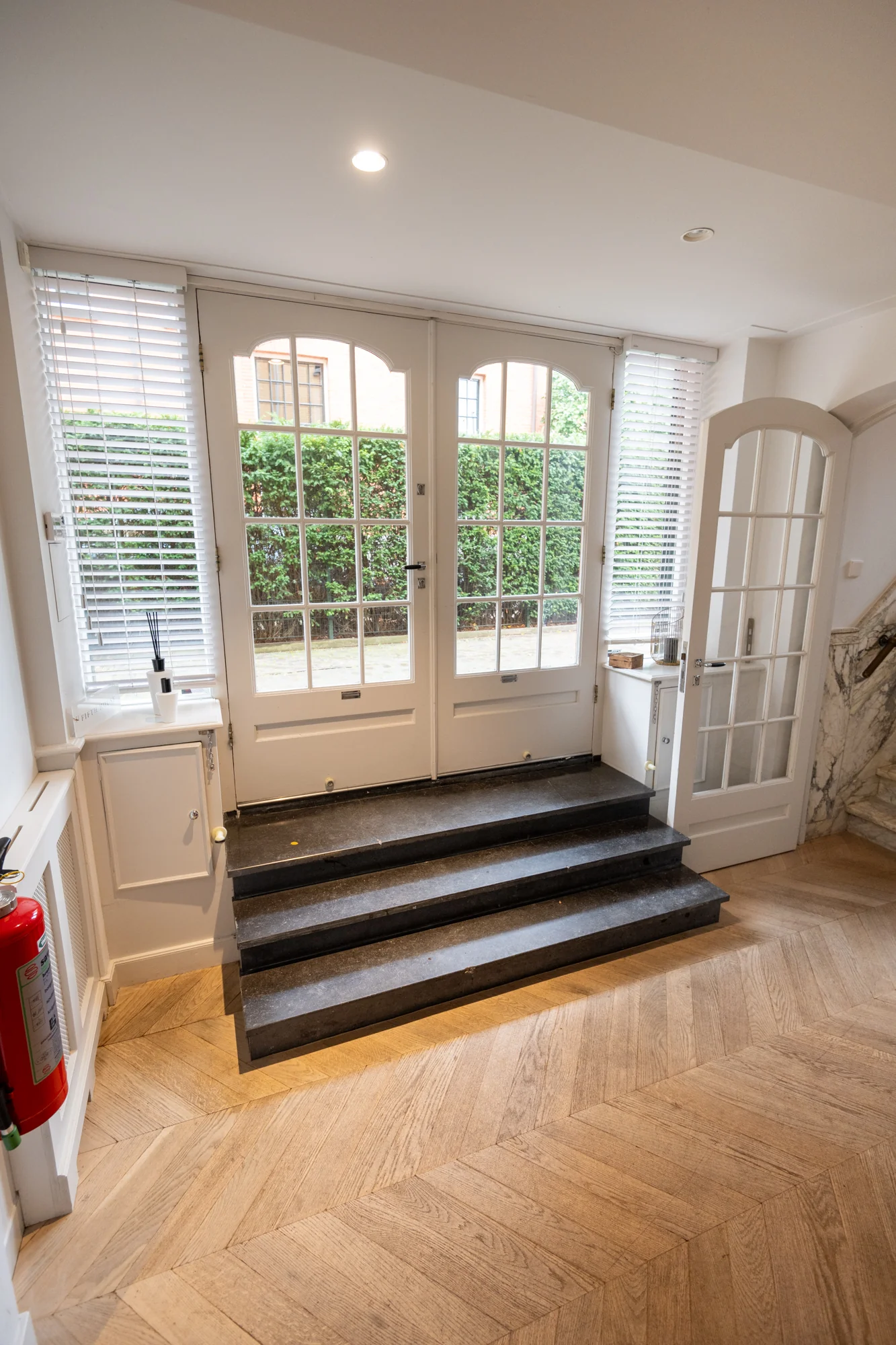 Ingang met dubbele glazen deuren aan de Hobbemastraat, gezien vanaf een houten visgraatvloer en zwarte stenen traptreden.