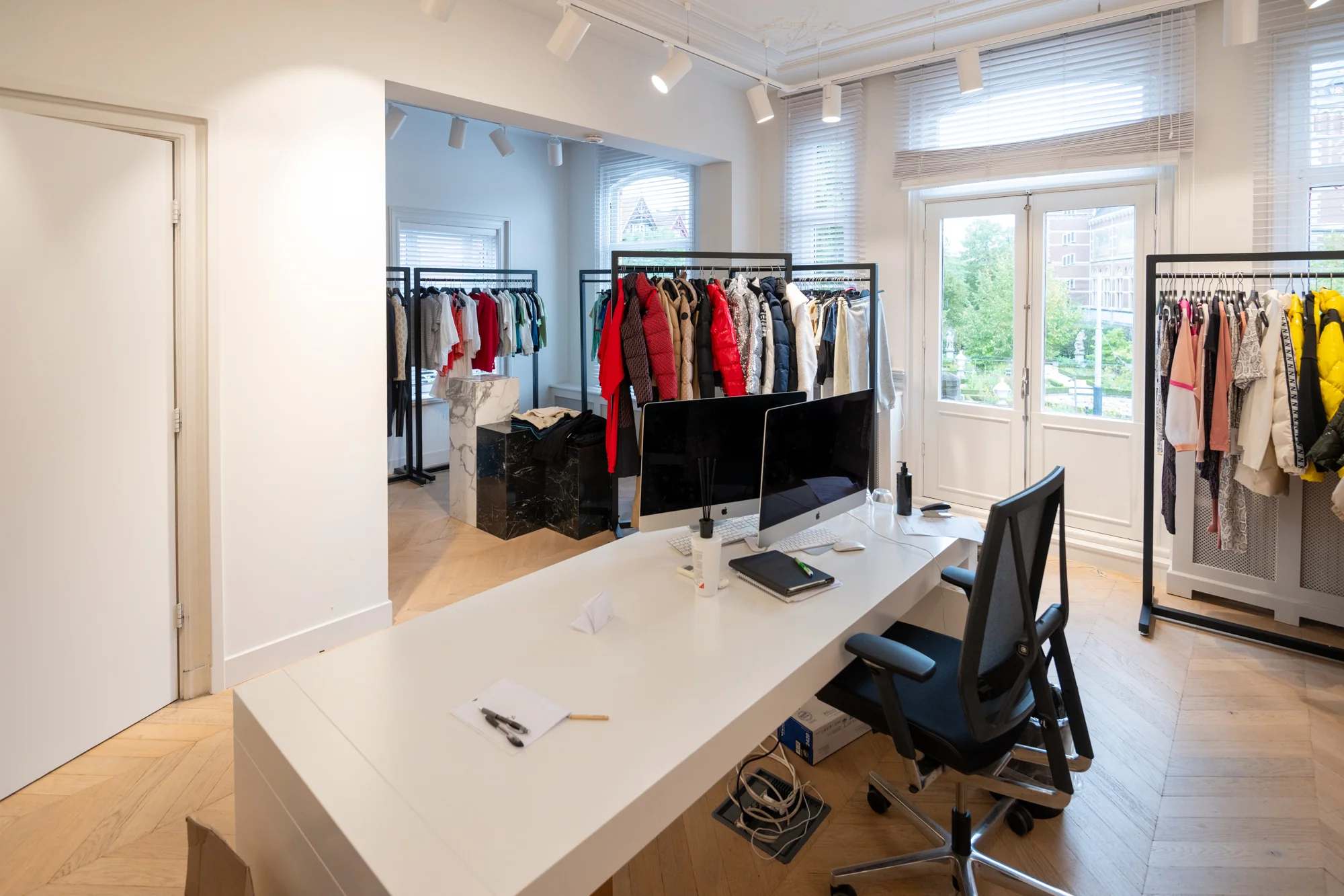 Modern kantoor met kledingrekken, werkplek en uitzicht op de Hobbemastraat.