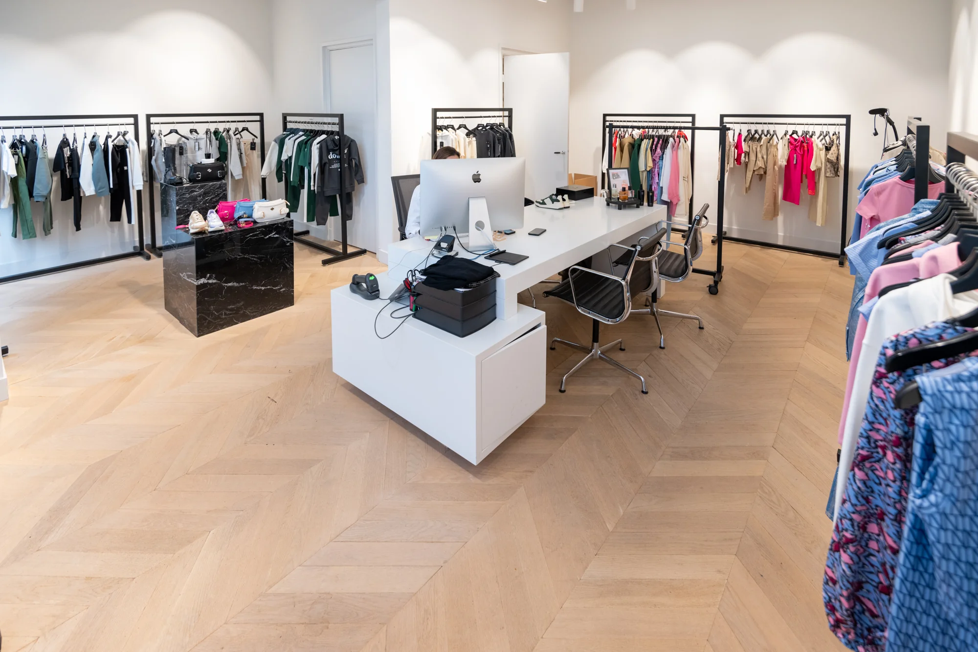 Moderne kledingwinkel aan de Hobbemastraat met strakke inrichting, kledingrekken en een centraal bureau met computer.