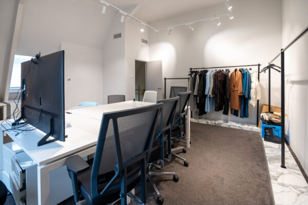 Modern kantoor aan de Hobbemastraat met bureaus, bureaustoelen en een kledingrek met diverse jassen en outfits.