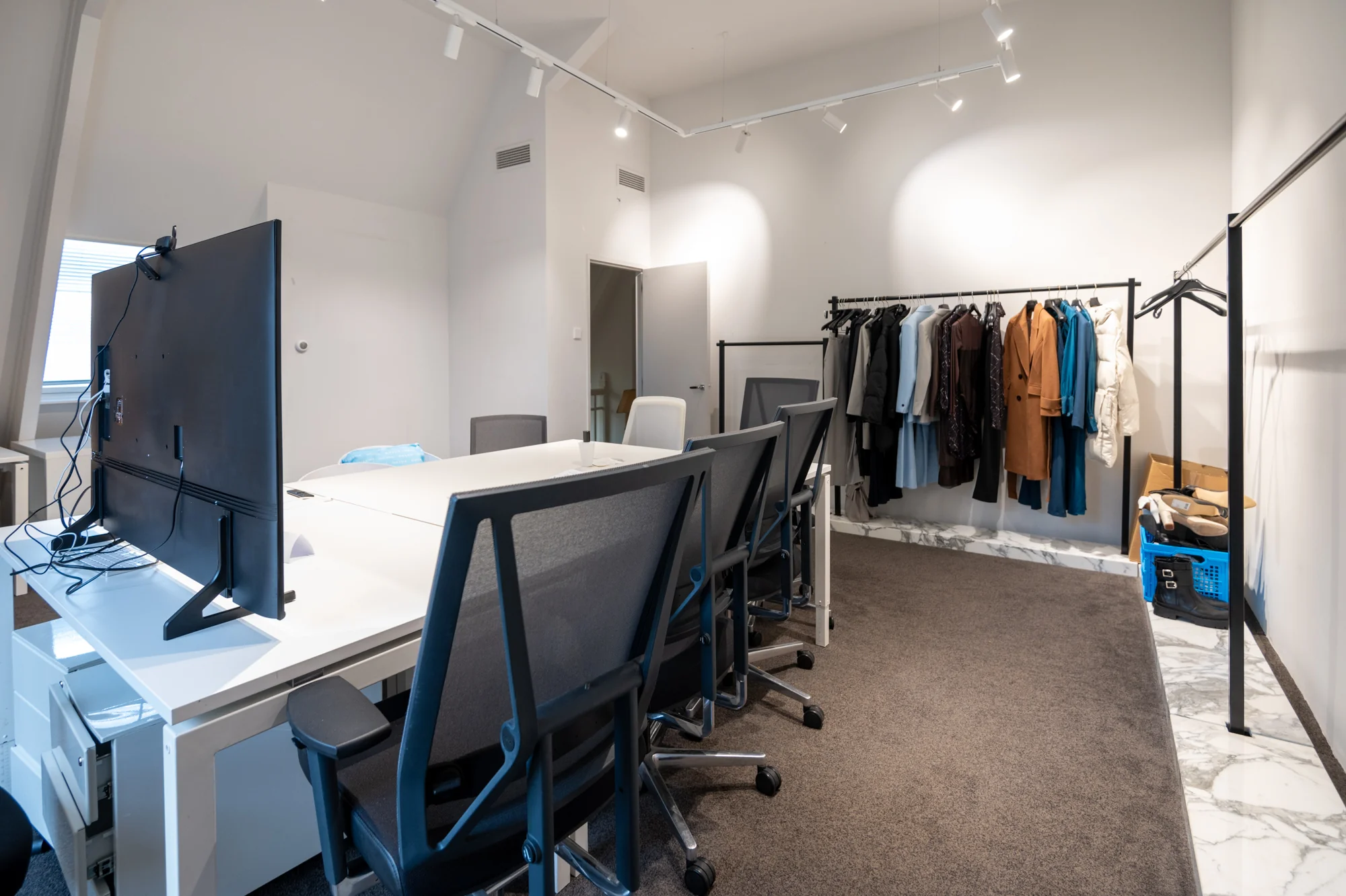 Modern kantoor aan de Hobbemastraat met bureaus, bureaustoelen en een kledingrek met diverse jassen en outfits.