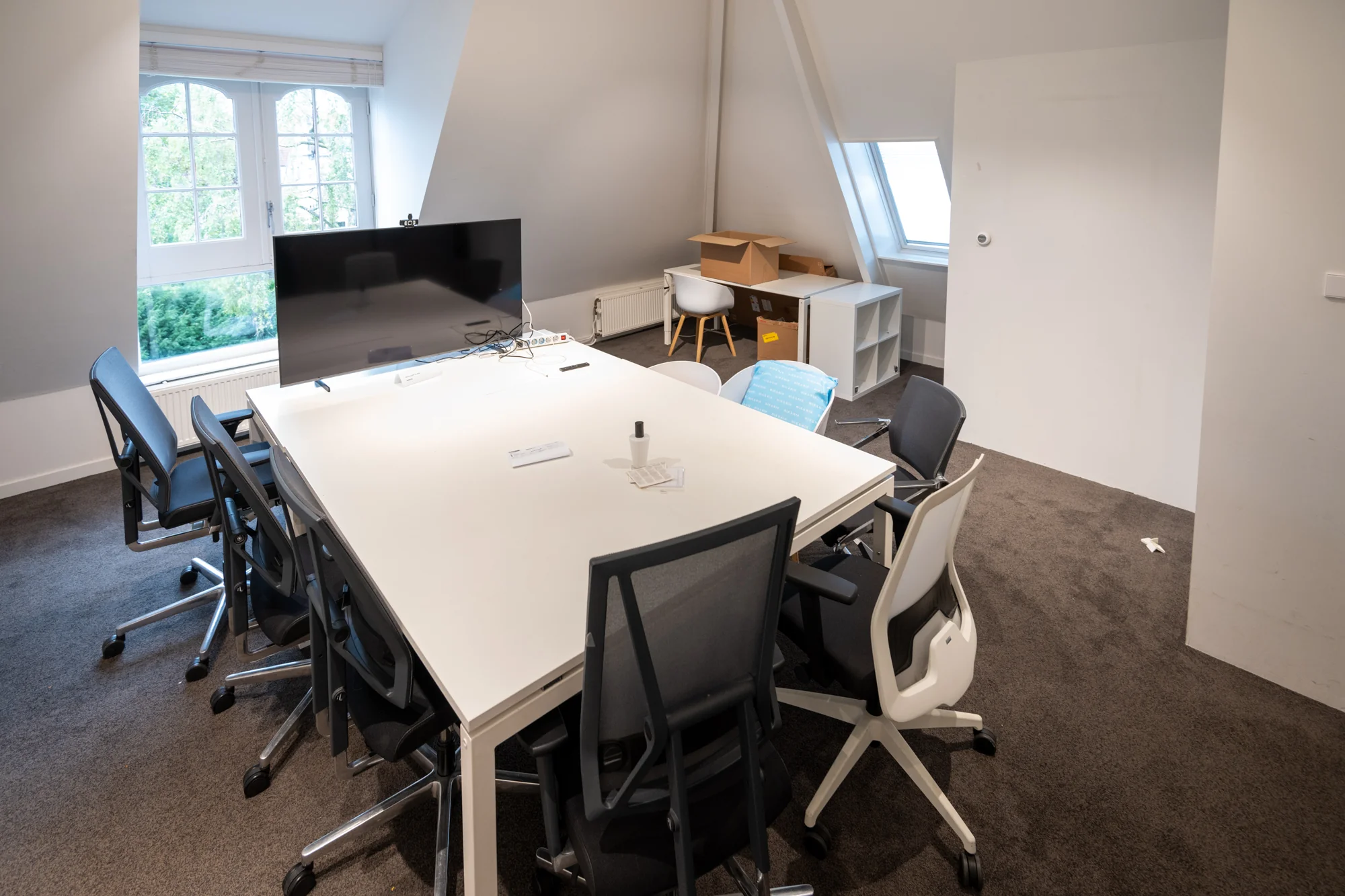 Vergaderruimte op de Hobbemastraat met een witte tafel, bureaustoelen, televisie en dakramen.