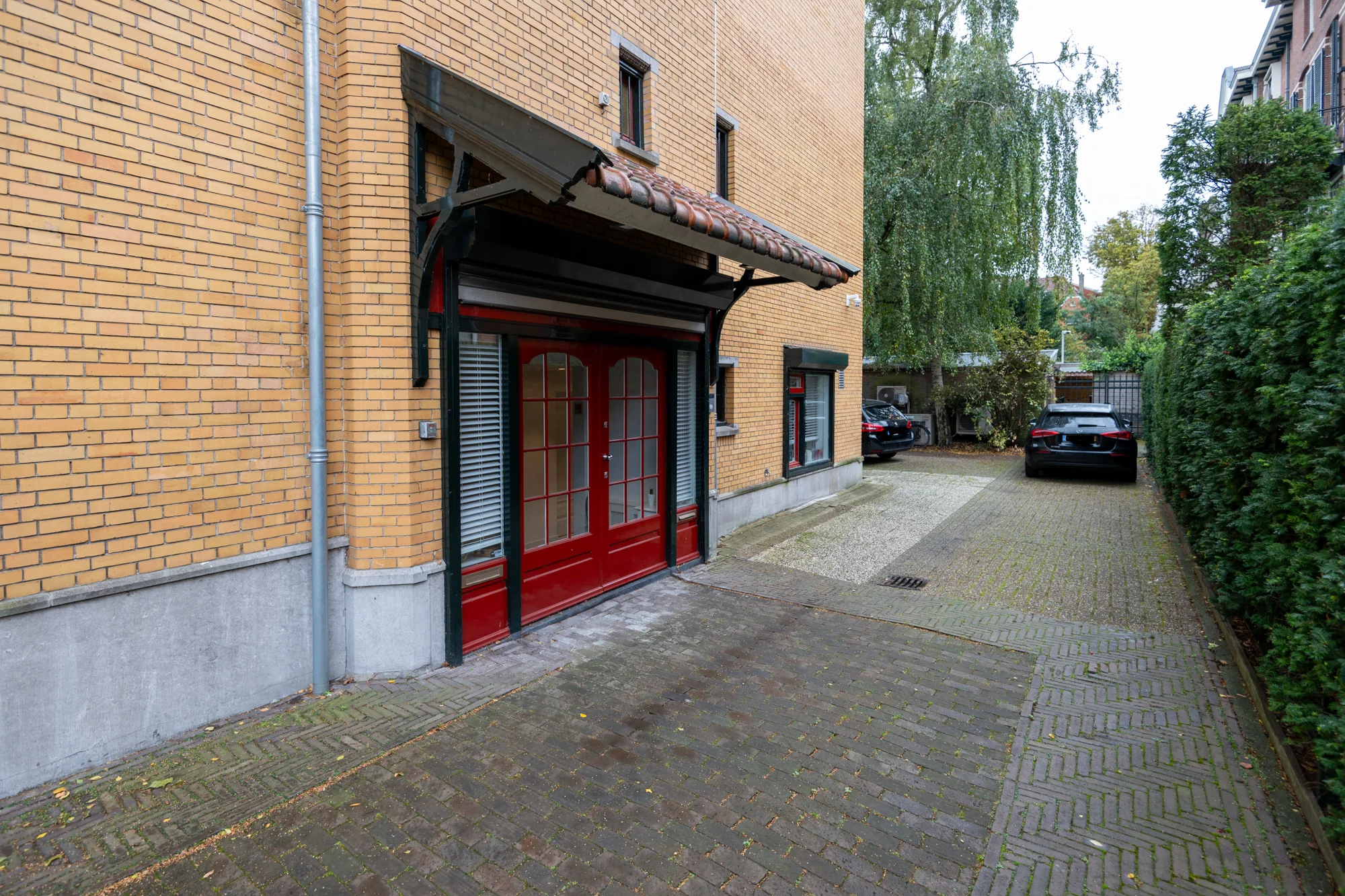 Ingang met rode deuren aan een geel bakstenen gebouw aan de Hobbemastraat, met oprit en geparkeerde auto's.