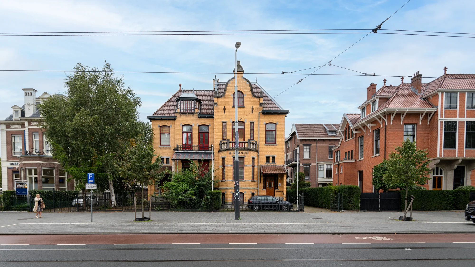 Gele bakstenen villa met het opschrift "Brands" aan de Hobbemastraat, geflankeerd door statige herenhuizen.