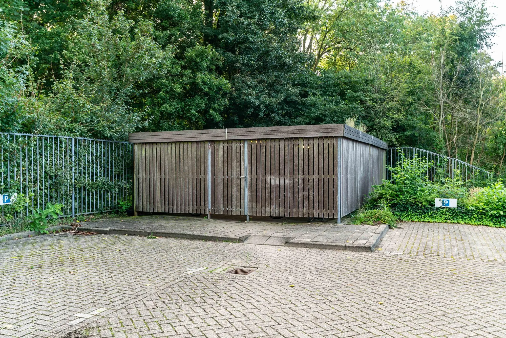 Houten fietsenstalling bij Delftechpark omringd door groen en een hekwerk.