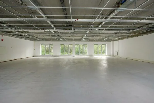 Lege kantoorruimte in Delftechpark met onafgewerkt plafond en grote ramen die uitkijken op groen.