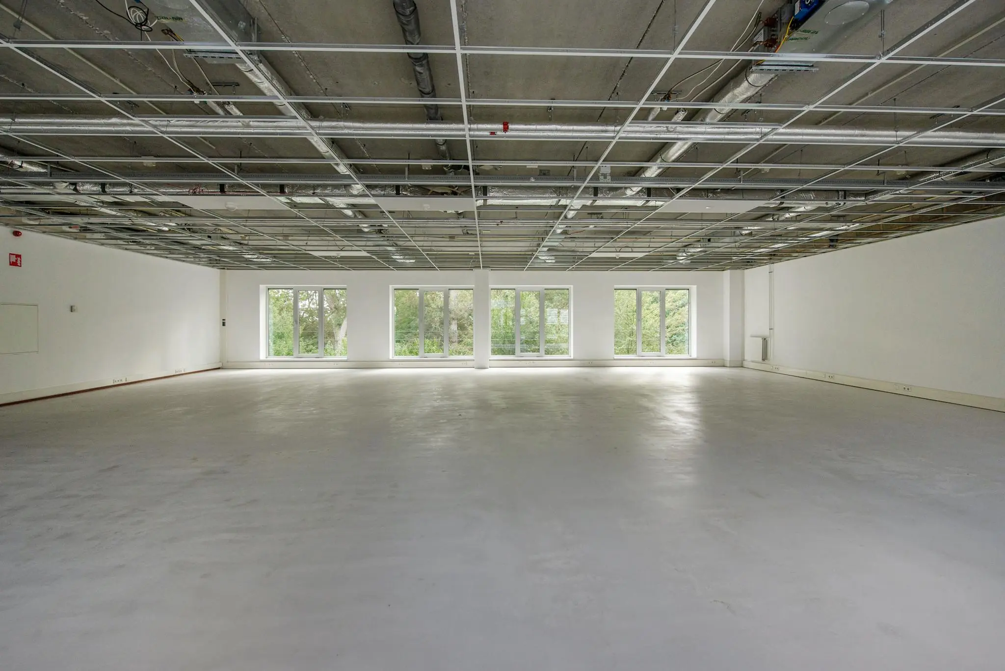 Lege kantoorruimte in Delftechpark met onafgewerkt plafond en grote ramen die uitkijken op groen.