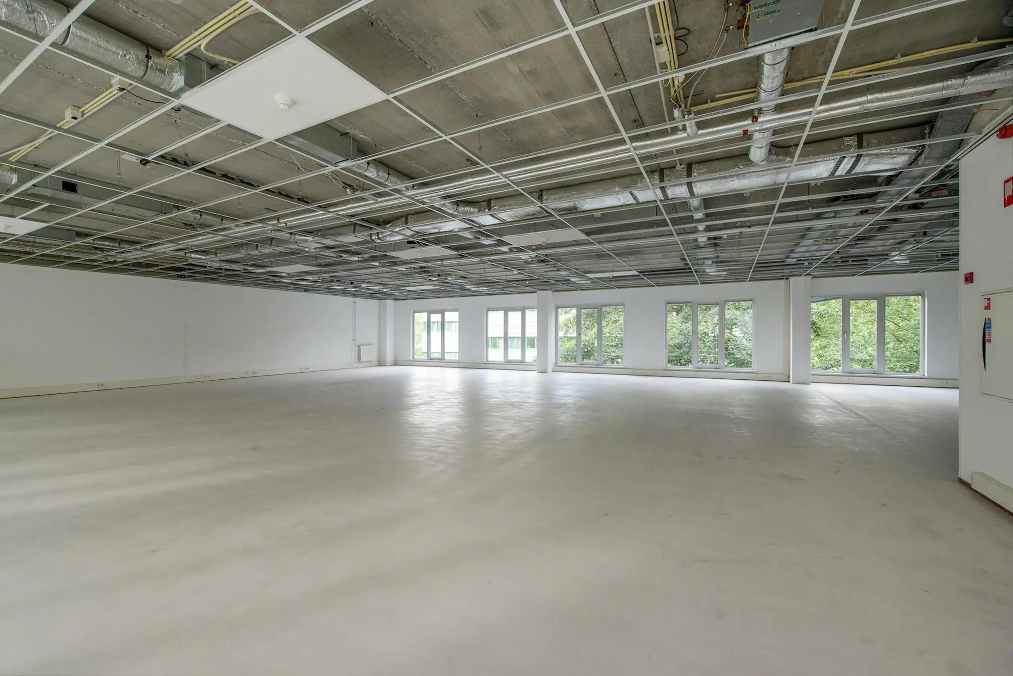 Leeg, licht en ruim kantoorinterieur in Delftechpark met onafgewerkt plafond en grote ramen.