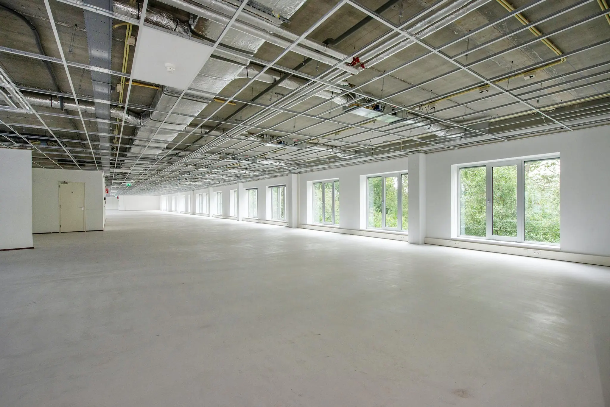 Leeg kantoorpand in Delftechpark met onafgewerkt plafond en grote ramen aan de rechterzijde.