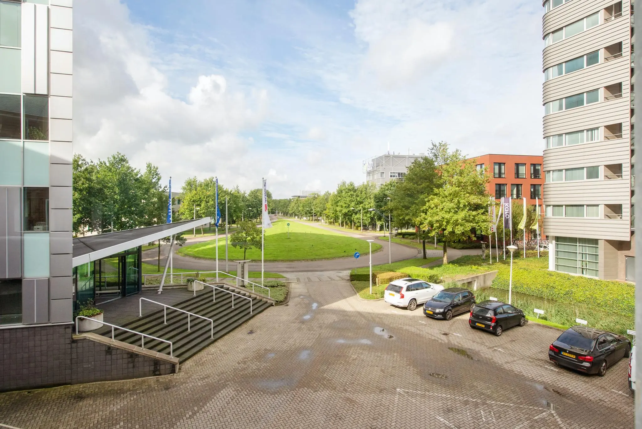 Bedrijventerrein Delftechpark met moderne kantoorgebouwen, geparkeerde auto's en een rotonde omgeven door groen.