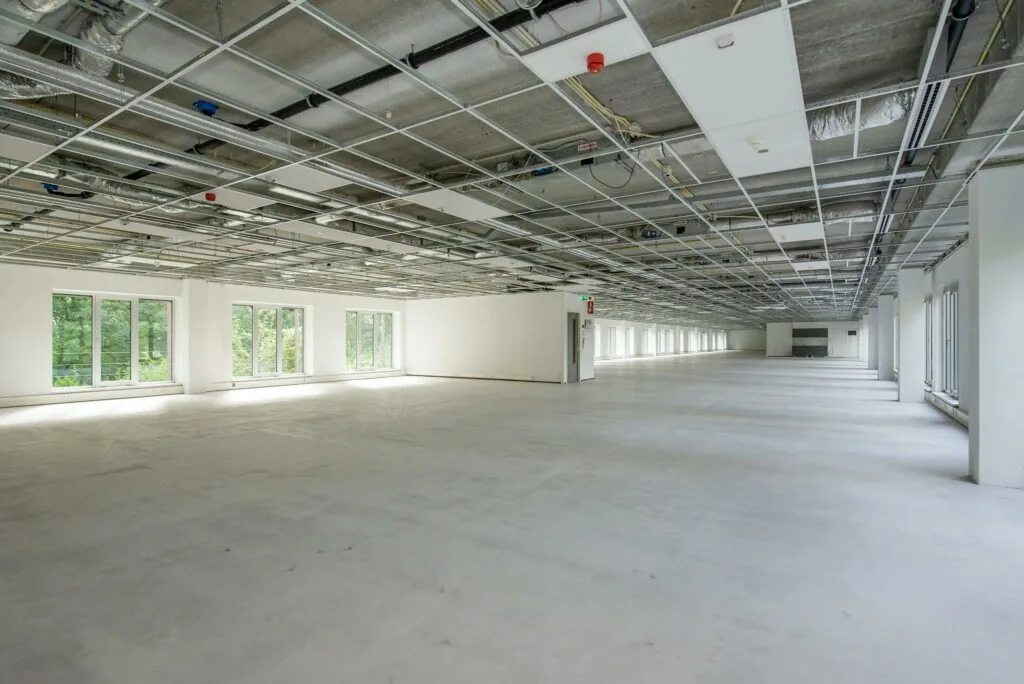 Leeg en ruim kantoorpand op Delftechpark met onafgewerkt plafond en grote ramen langs de zijkant.