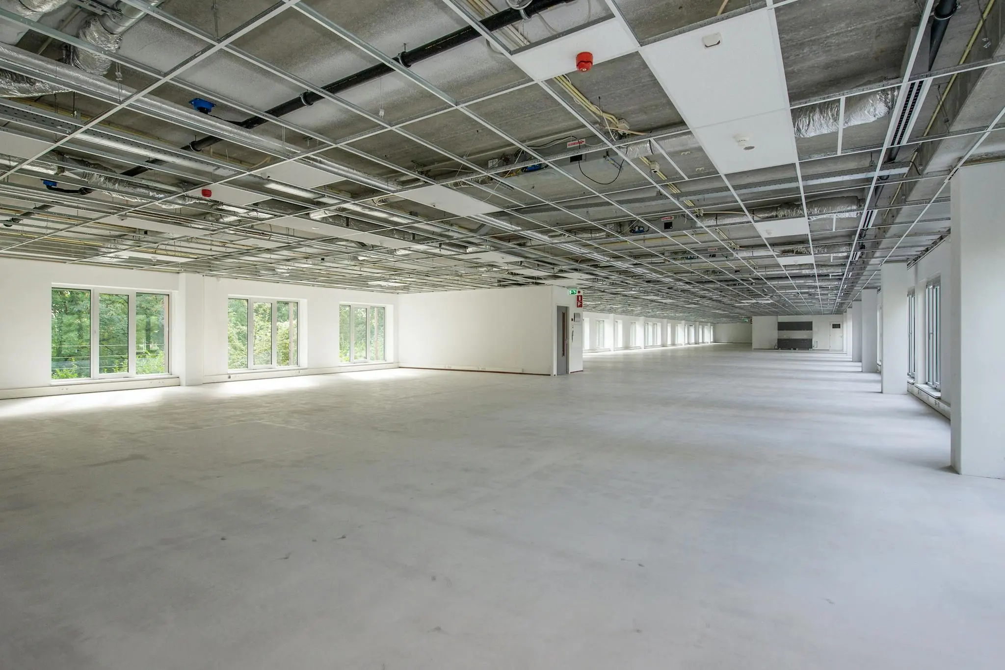 Leeg en ruim kantoorpand op Delftechpark met onafgewerkt plafond en grote ramen langs de zijkant.