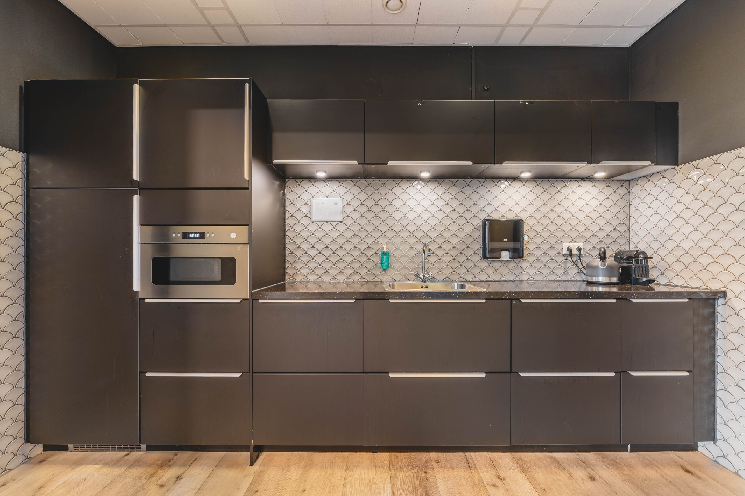 Moderne keuken met donkere kasten, een ingebouwde oven en een betegelde achterwand met visgraatmotief.