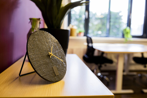 Een klok met een textuurpatroon staat op een houten tafel in een modern kantoor.