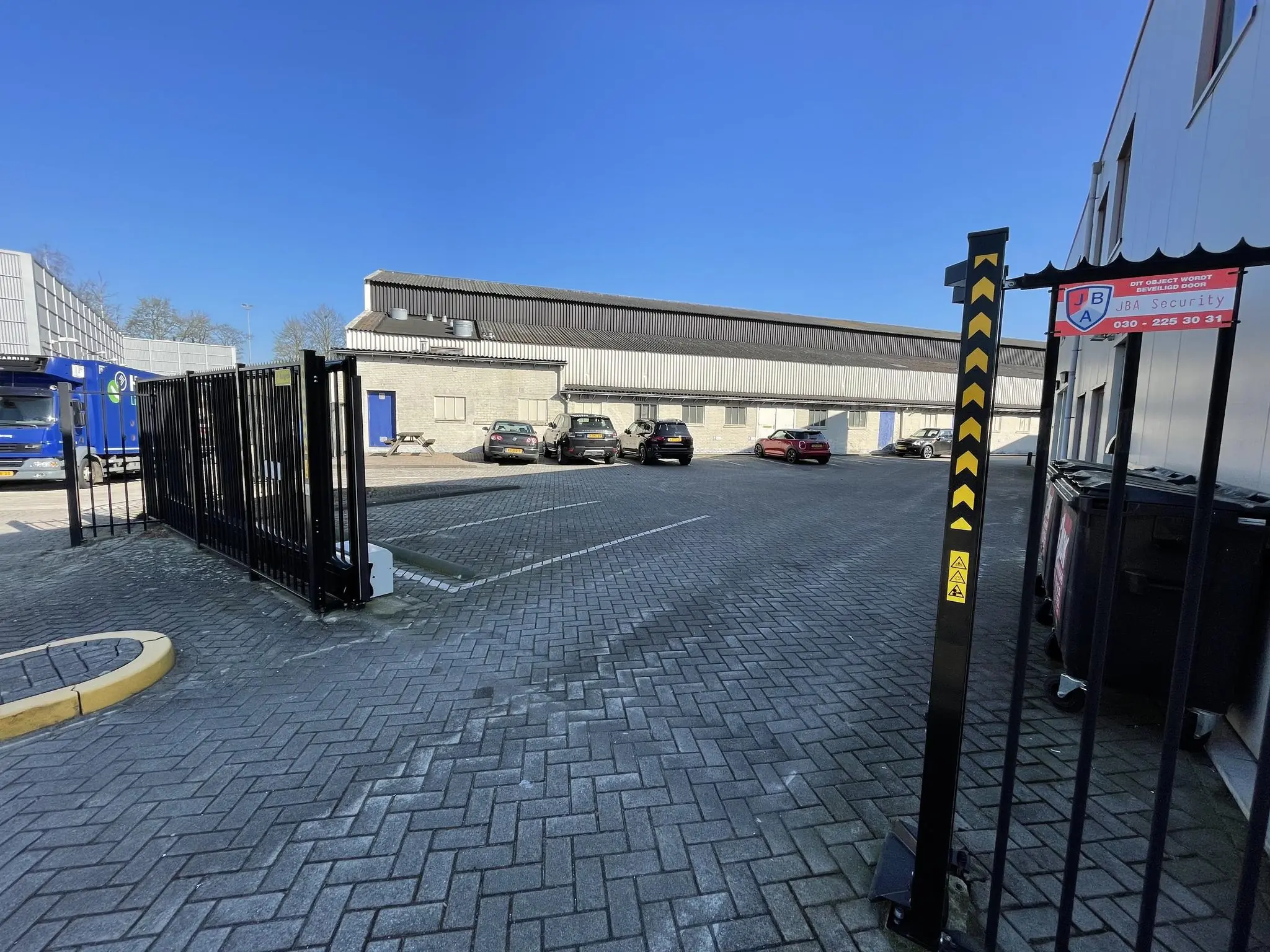 Bedrijfsterrein aan de Kwekerijweg met parkeervakken, beveiligingshek en borden van JBA Security.