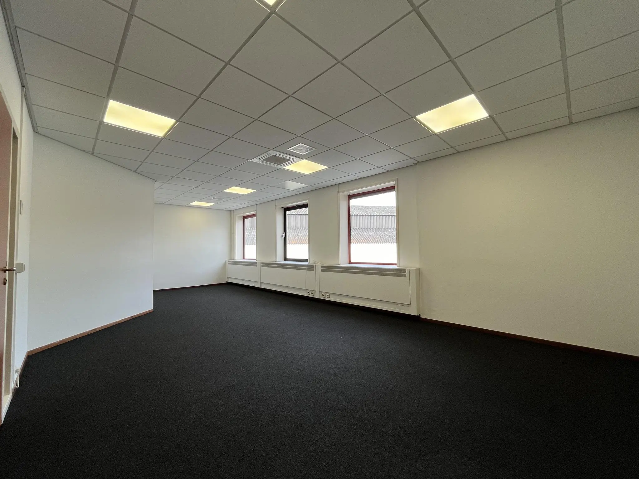 Leeg kantoorruimte aan de Kwekerijweg met witte muren, systeemplafond en donkere vloerbedekking.