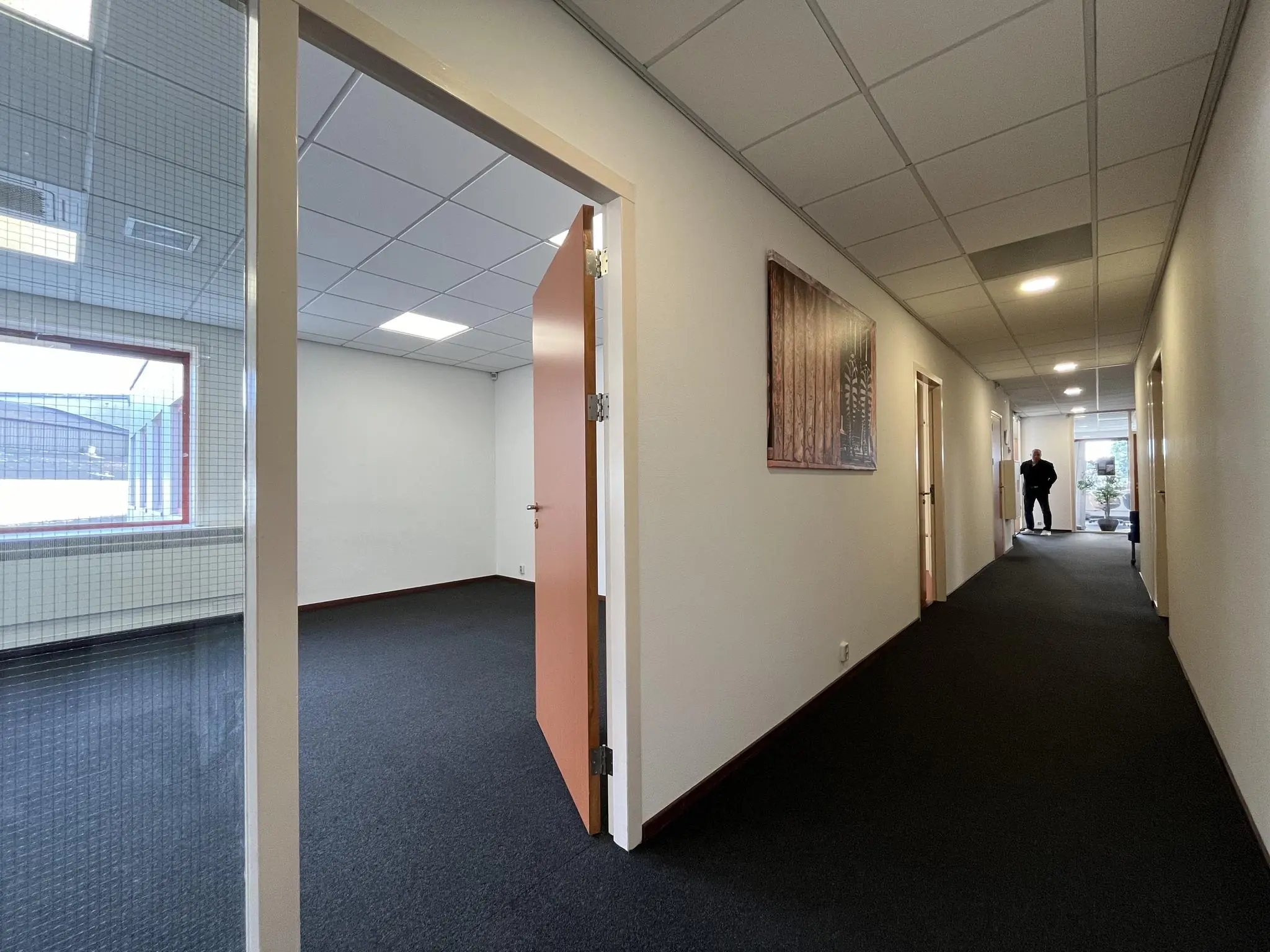 Gang in een kantoorpand aan de Kwekerijweg met openstaande deur naar een leeg kantoor en een persoon aan het einde van de gang.