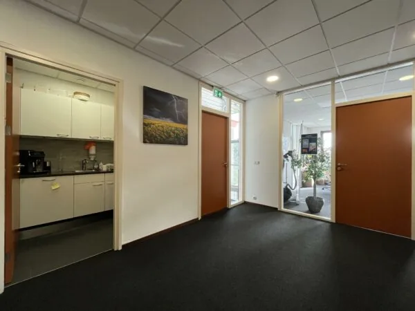 Ingang van een kantoorruimte aan de Kwekerijweg met zicht op een keuken, gesloten deuren en een fitnessruimte.