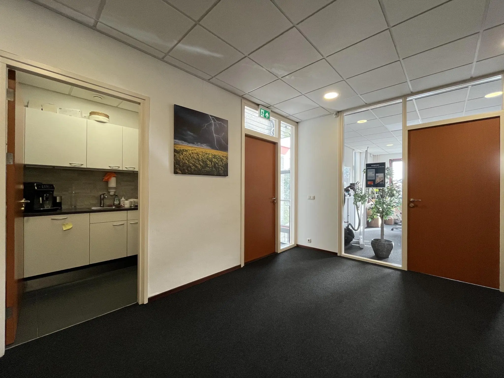 Ingang van een kantoorruimte aan de Kwekerijweg met zicht op een keuken, gesloten deuren en een fitnessruimte.
