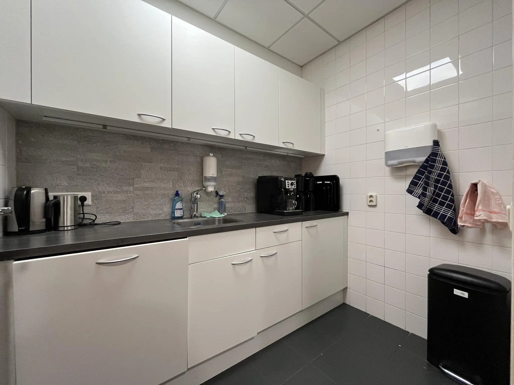 Moderne bedrijfskeuken aan de Kwekerijweg met witte kasten, koffieapparaten en schoonmaakmiddelen.