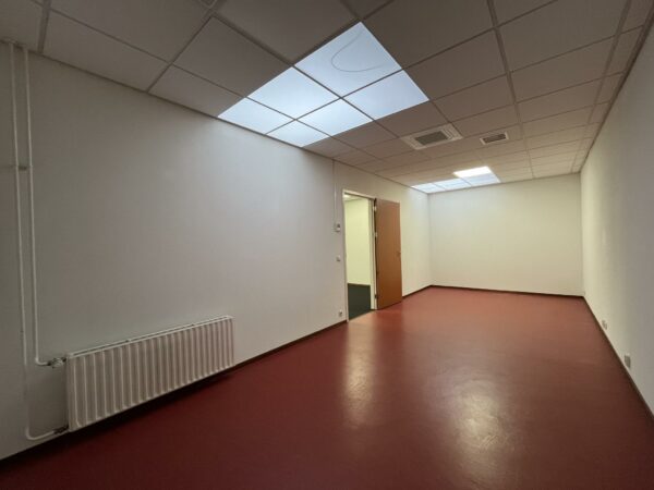 Lege kantoorruimte aan de Kwekerijweg met rode vloer, systeemplafond en openstaande houten deur.