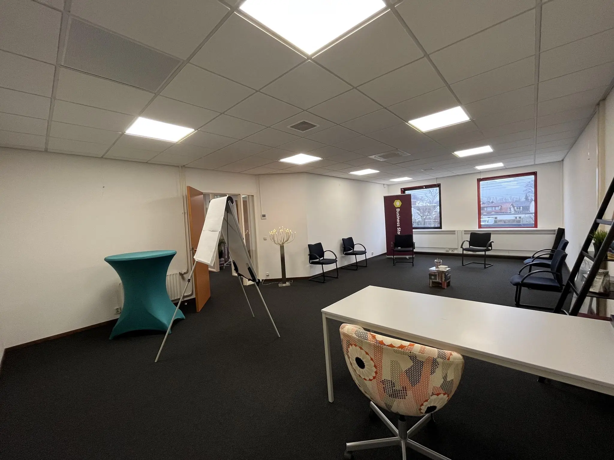 Vergaderruimte aan de Kwekerijweg met stoelen in kringopstelling, een flip-over en een bureau met kleurrijke stoel.