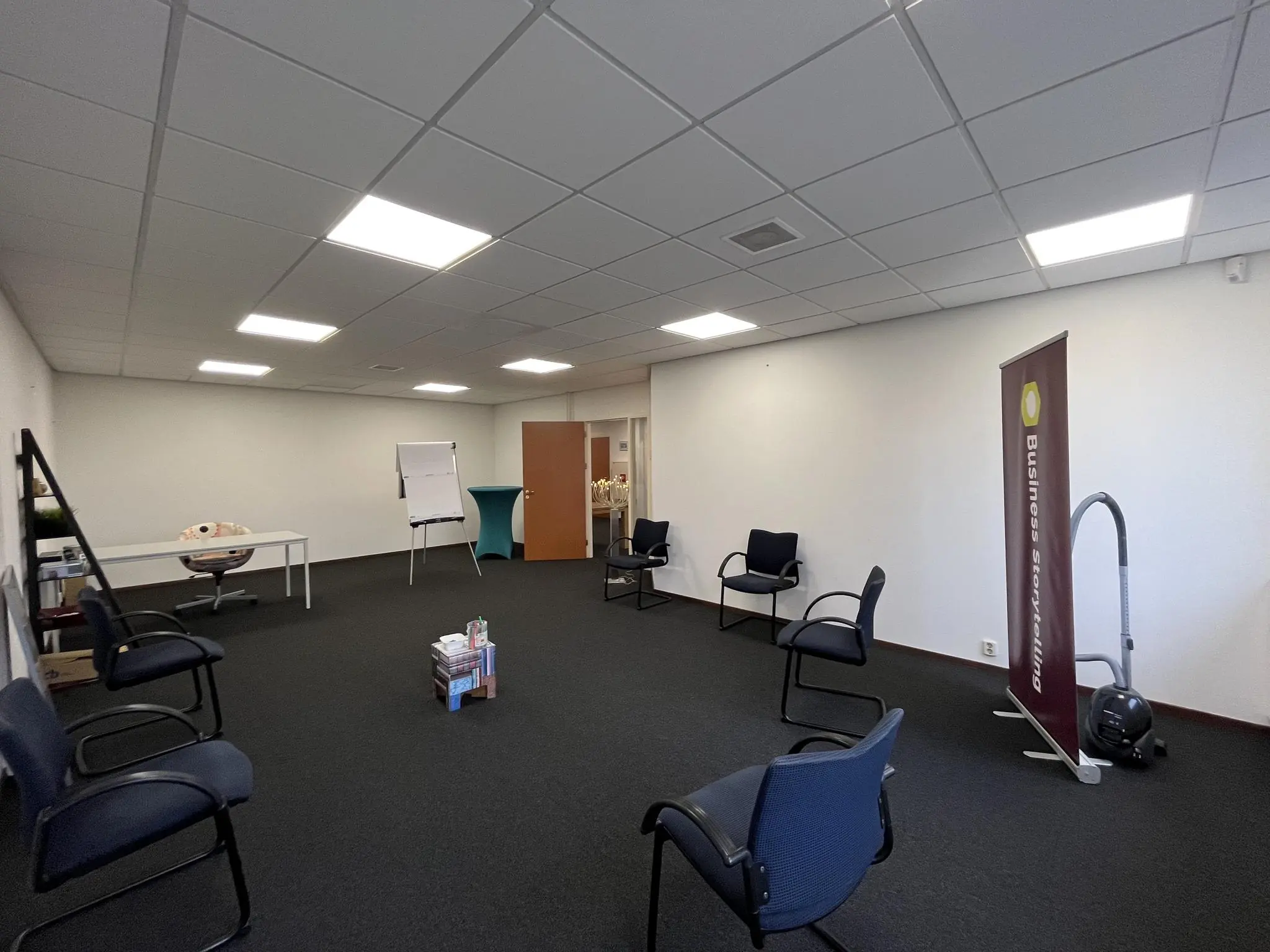 Vergaderruimte met stoelen in een kringopstelling, flip-over, boekenstapel en een banner met de tekst "Business Storytelling".