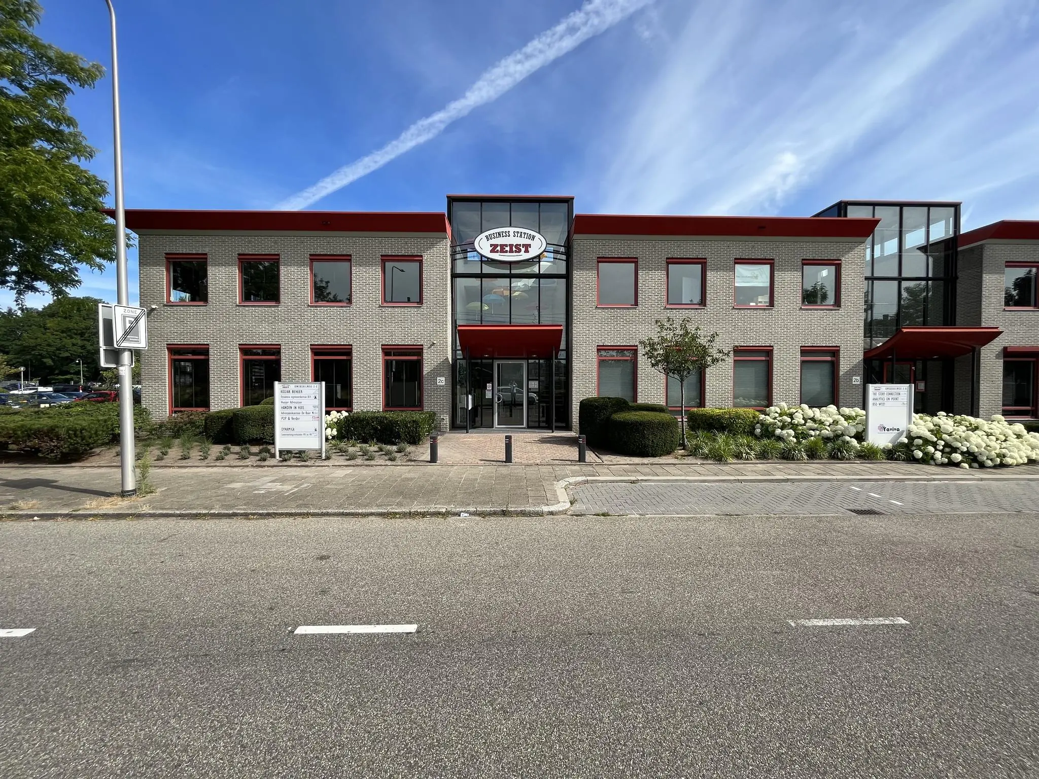 Bedrijfspand aan de Kwekerijweg in Zeist met rode accenten en omliggende beplanting, gefotografeerd vanaf de straat.