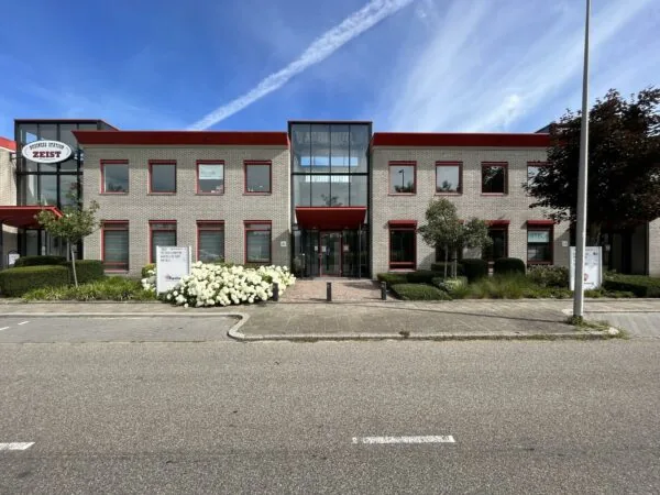 Vooraanzicht van het kantoorgebouw Business Station Zeist aan de Kwekerijweg met rode kozijnen en verzorgde beplanting.