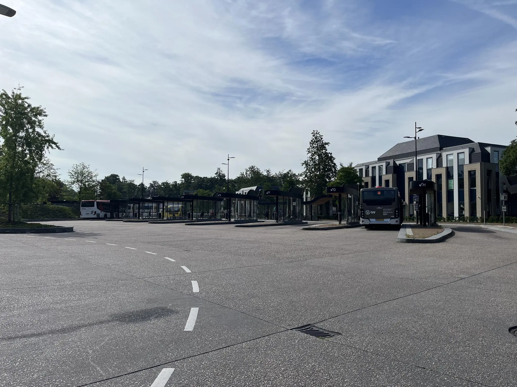 Bushalte aan de Kwekerijweg met meerdere wachtende bussen en een modern gebouw op de achtergrond.