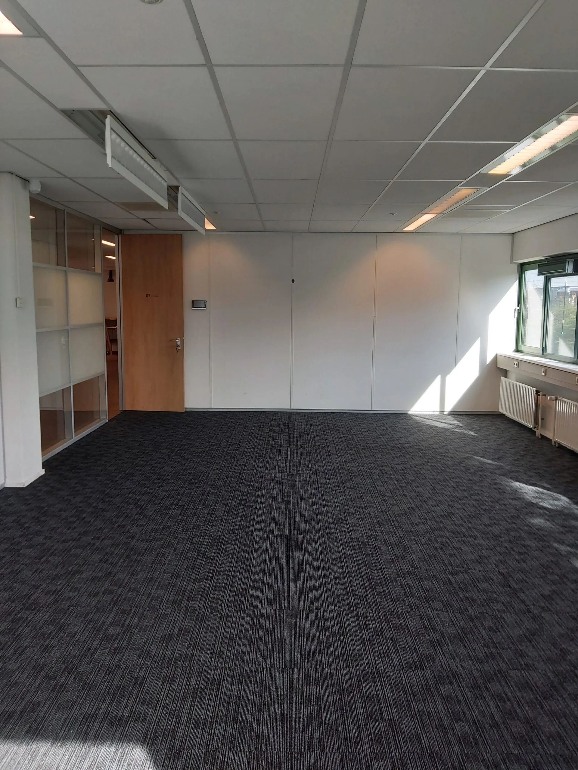 Leegstaande kantoorruimte met tapijtvloer, systeemplafond en grote ramen aan de Zekeringstraat 43 in Amsterdam.
