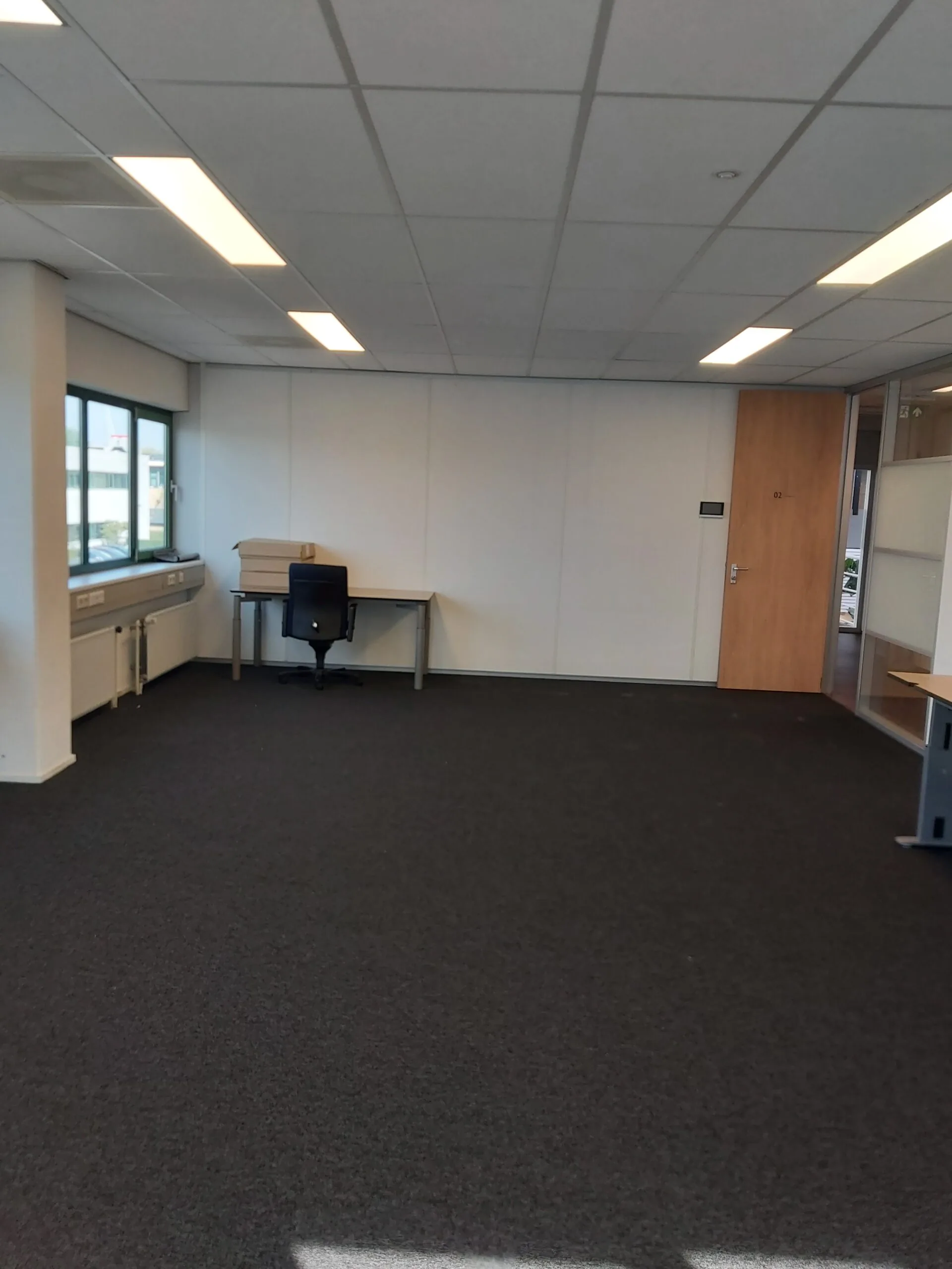 Lege kantoorruimte met tapijtvloer, systeemplafond en enkele bureaus aan de Zekeringstraat 43 in Amsterdam.