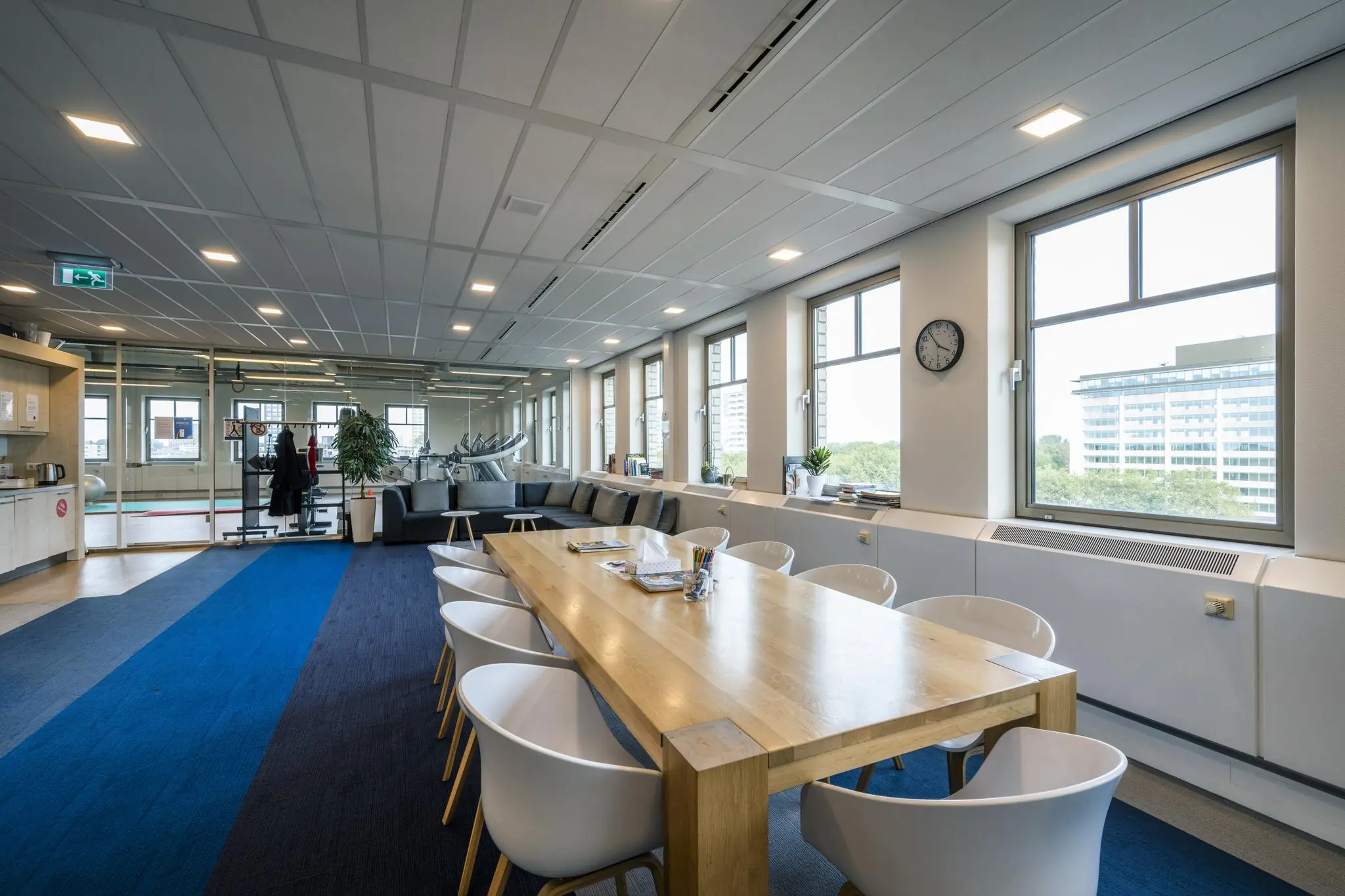 Moderne kantoorruimte aan de Derkinderenstraat met vergadertafel, zithoek en zicht op fitnessapparaten.