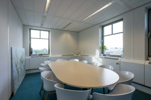 Vergaderruimte met ovale tafel, twaalf witte stoelen en uitzicht op de Derkinderenstraat.