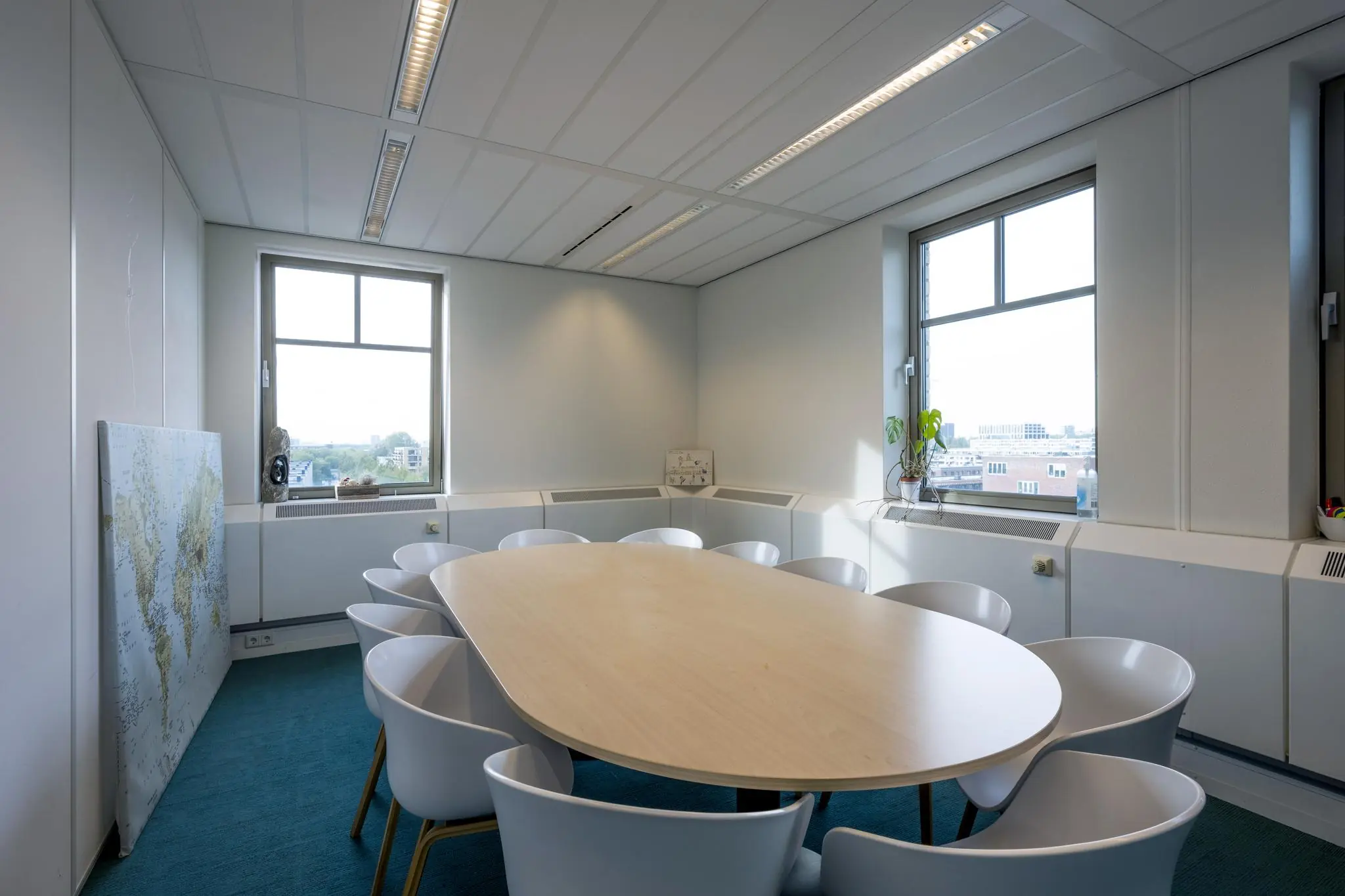 Vergaderruimte met ovale tafel, twaalf witte stoelen en uitzicht op de Derkinderenstraat.