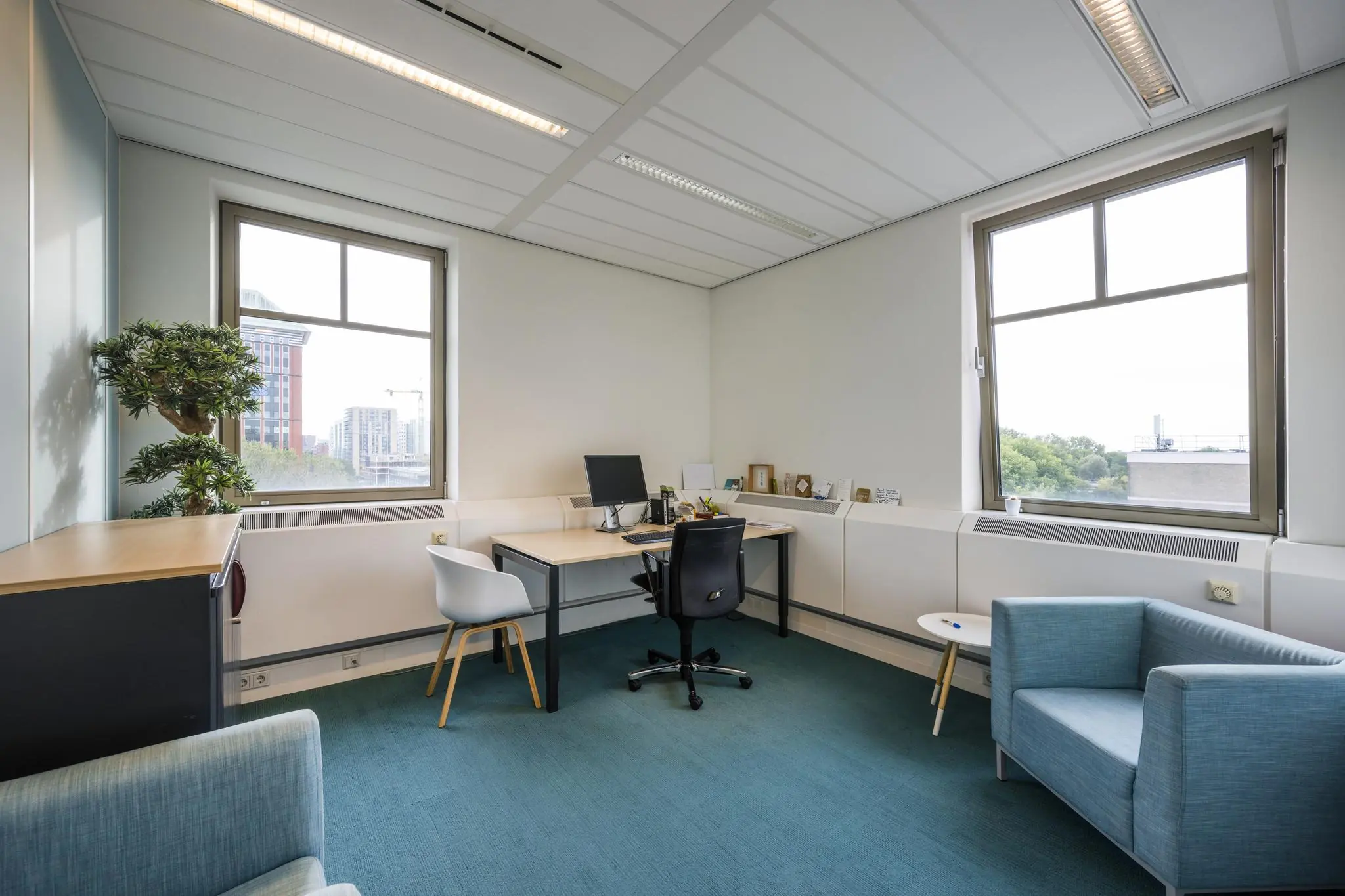 Modern ingericht kantoor aan de Derkinderenstraat met bureau, zithoek en uitzicht op de stad.