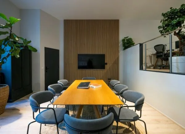 Vergaderruimte aan de Sarphatistraat met houten tafel, moderne stoelen, een flatscreen en een houten wandpaneel.