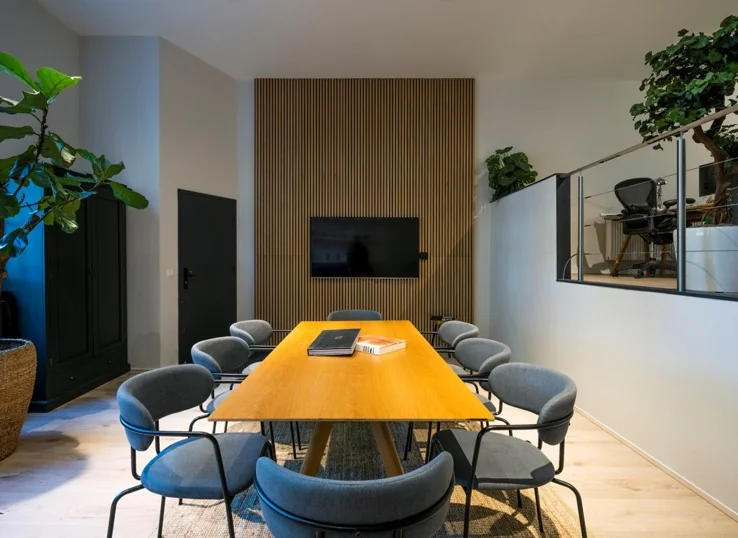 Vergaderruimte aan de Sarphatistraat met houten tafel, moderne stoelen, een flatscreen en een houten wandpaneel.