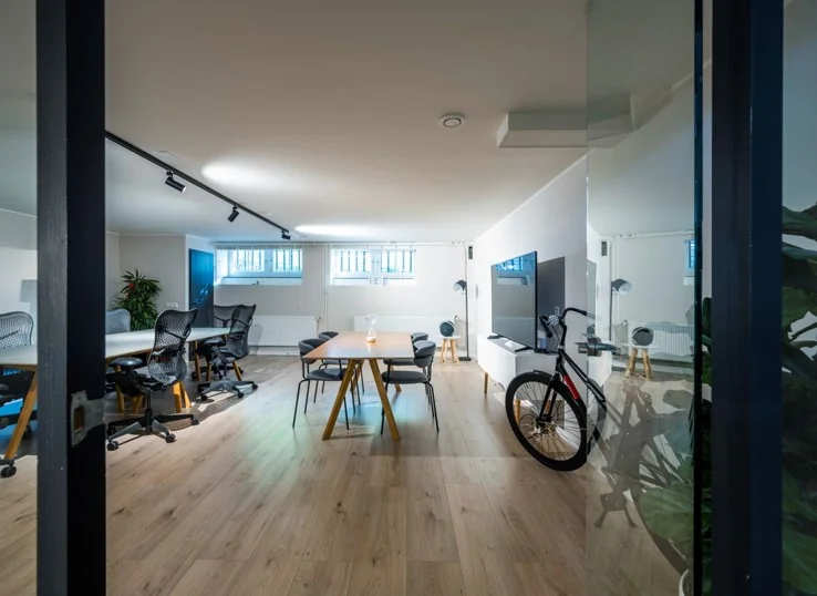 Modern ingericht kantoor aan de Sarphatistraat met houten vloer, vergadertafel, bureaustoelen en een fiets tegen de muur.
