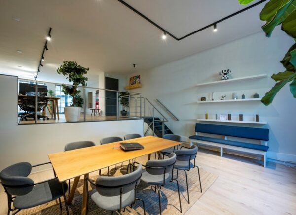 Modern ingerichte vergaderruimte aan de Sarphatistraat met houten tafel, grijze stoelen en een verhoogd zitgedeelte.