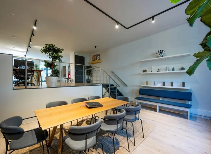 Modern ingerichte vergaderruimte aan de Sarphatistraat met houten tafel, grijze stoelen en een verhoogd zitgedeelte.