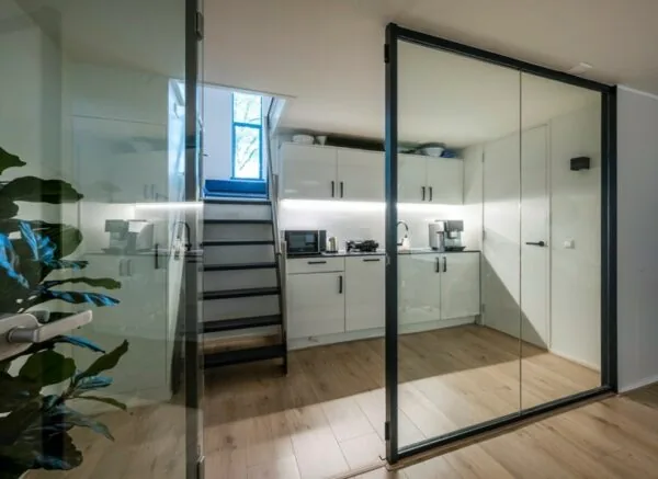 Moderne witte kitchenette aan de Sarphatistraat met glazen schuifdeuren en houten vloer.