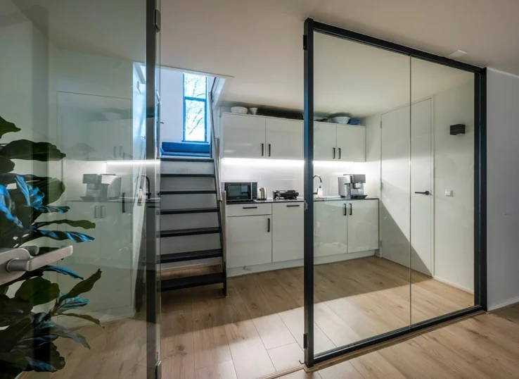 Moderne witte kitchenette aan de Sarphatistraat met glazen schuifdeuren en houten vloer.