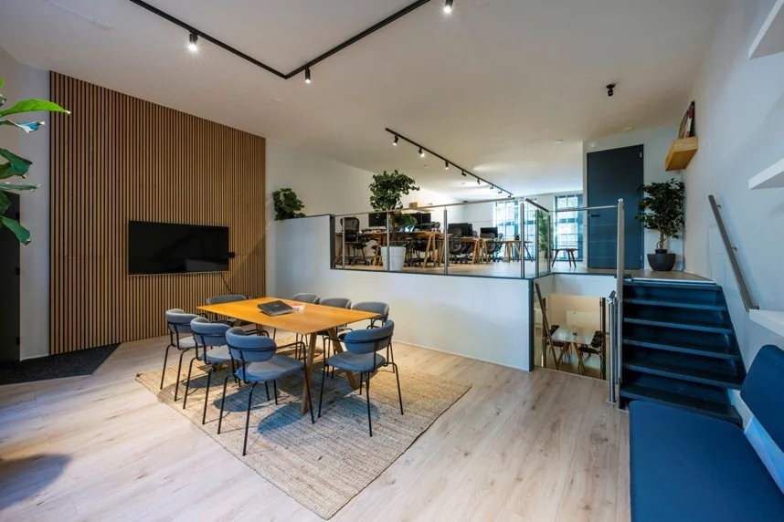 Moderne kantoorruimte aan de Sarphatistraat met een vergadertafel, houten wand met scherm, split-level indeling en werkplekken op het bovenniveau.