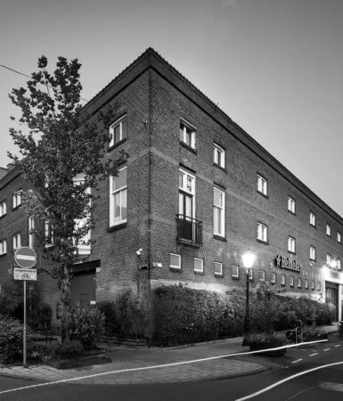 Zwart-witfoto van een hoekpand aan de Ruysdaelkade in Amsterdam met Heineken-logo op de gevel.
