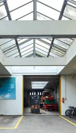 Doorkijk naar een opslagruimte aan de Ruysdaelkade met glazen dak, een heftruck en een Heineken-bord.