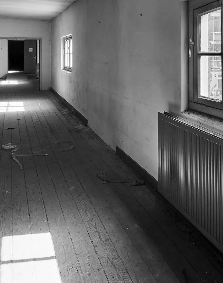 Zwart-witfoto van een leeg en vervallen gangpad met houten vloer aan de Ruysdaelkade, verlicht door invallend daglicht.