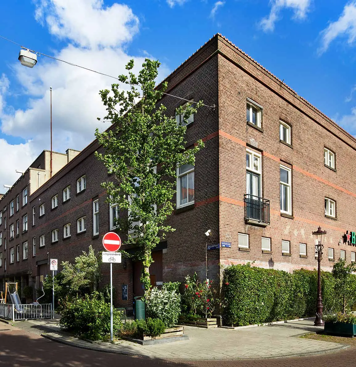 Op de hoek van de Ruysdaelkade staat een groot roodbruinen bakstenen woongebouw met planten en een eenrichtingsverkeer-bord op de voorgrond.